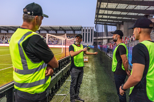 Security guards discussing with each other while standing outside football pitch.