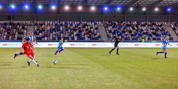 Soccer player in blue jersey in the air heading the ball. Stadium in the background.