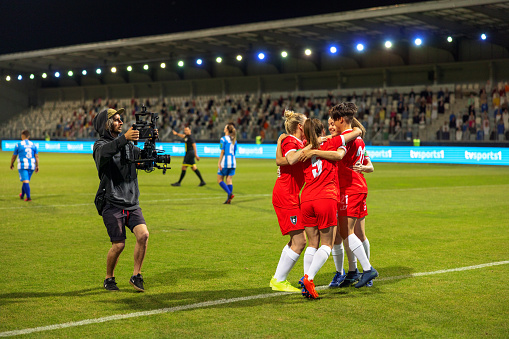 Photographer taking picture of smiling female football players celebrating after winning match on football pitch.
