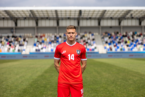 Portrait of male football player in red jersey standing on football pitch during match.