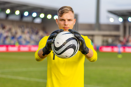 Portrait of goalkeeper holding football while standing on football pitch.
