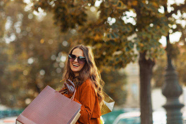 happy elegant female in brown trench coat with shopping bags stock photo