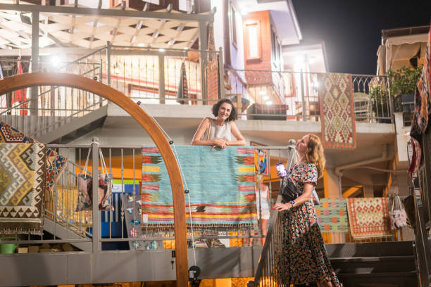 две веселые женщины сидят на ступеньках группы ковровых магазинов. - rug shop стоковые фото и изображения