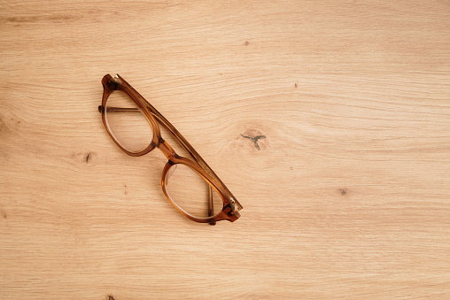 Brown eyeglasses on a wooden surface with copy space