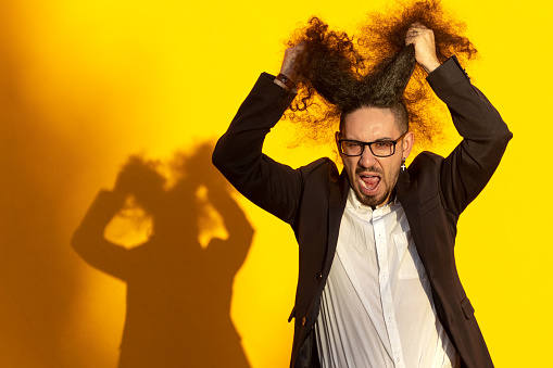 portrait of stressed long-haired businessman pulling his hair out over yellow background