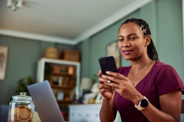 istock An African woman text messages on her phone while working on her laptop. 1633981222