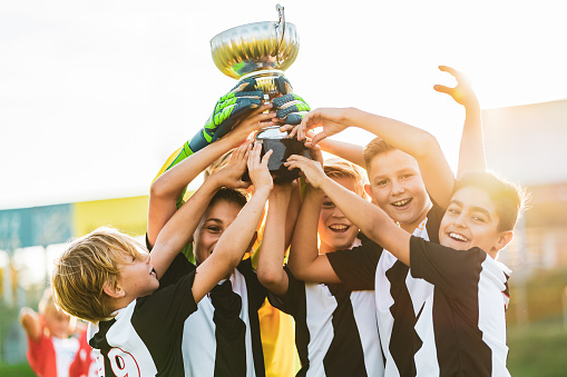 happy cheerful junior soccer players kids with first place trophy celebrating victory winning junior talent football match