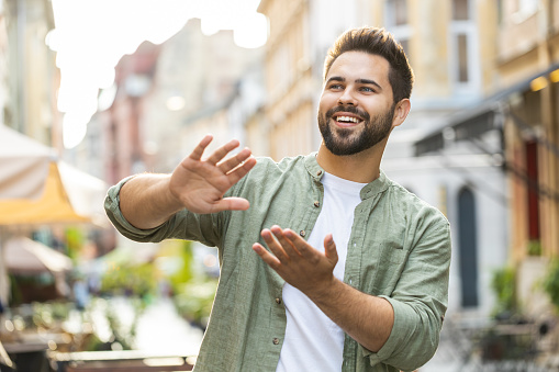 Cheerful rich bearded young man showing wasting throwing money around hand gesture, more tips earnings, big profit, win lottery, share, celebrate outdoors. Caucasian guy standing in urban city street
