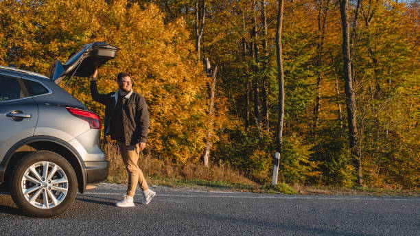 istock Autumn forest background with a smiling man closes his car. copy space 1634006571
