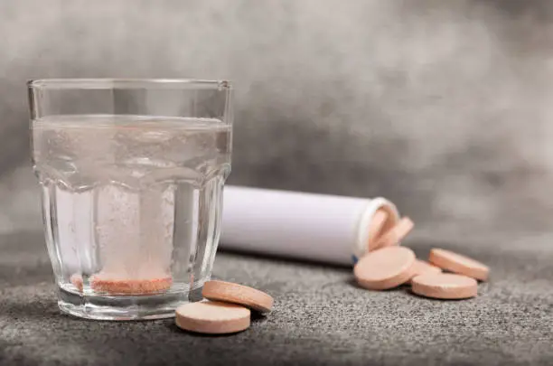 Photo of Effervescent tablet in a glass of water on a textured background. Vitamins. Health concept. Immunity drug. Space for copy. Space for text.