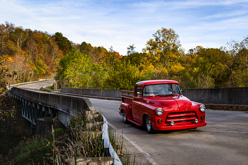 A red vintage truck cruising over a bridge during an autumn sunset.