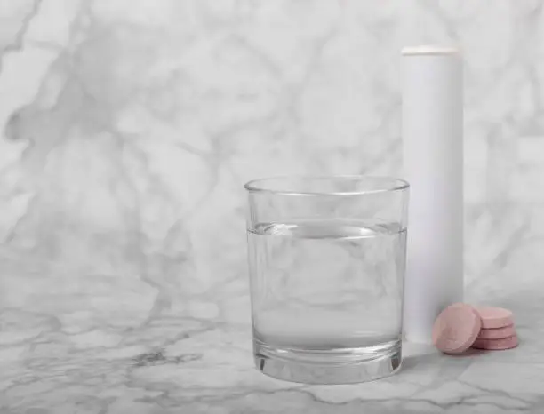 Photo of Effervescent tablet in a glass of water on a black textured background. Vitamins. Health concept. Immunity drug. Space for copy. Space for text.