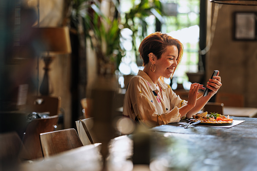 Young and happy Hispanic woman using a phone while having lunch in a restaurant.