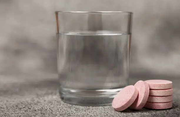 Photo of Effervescent tablet in a glass of water on a black textured background. Vitamins. Health concept. Immunity drug. Space for copy. Space for text.