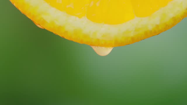 Orange with dripping clear juice on green background