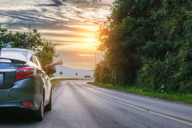 gesto del pollice in su dalla mano di una viaggiatrice su una strada asfaltata mentre avanza. concetto di viaggiare in automobile o noleggiare un'auto - automobile personale foto e immagini stock