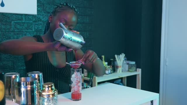 African black waitress prepares a cocktail on the bar of a pub