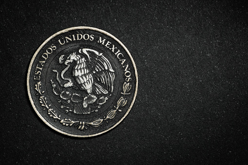 Coat of arms of the United Mexican States from a 10 pesos coin on a textured black surface. Shield that is also found on the flag of Mexico