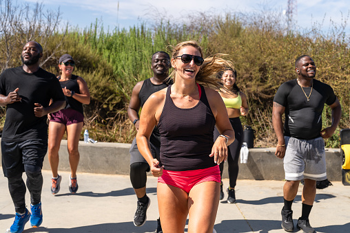 A White woman, sporting a pair of shades and red shorts, smiles as she's performing a cardio exercise during an outdoor workout session in Culver City, California.