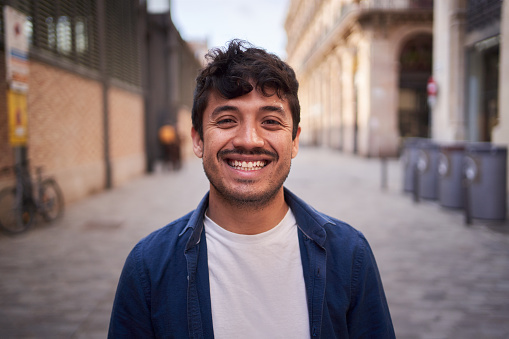 Portrait of happy young Latin man happy smiling friendly face on street. Male cheerful people with positive expression looking at camera in open air. Nice boy posing for photo outdoor