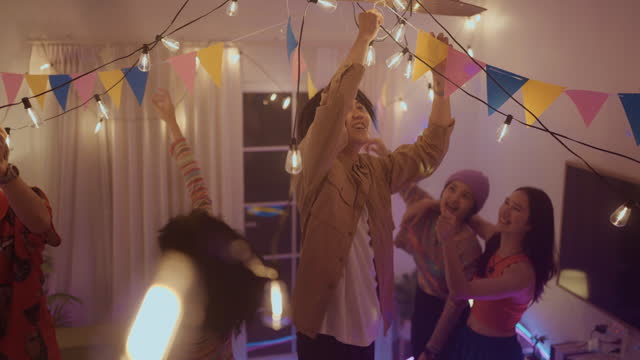 A group of asian friends are decorating a room with flags and lights to party at night.