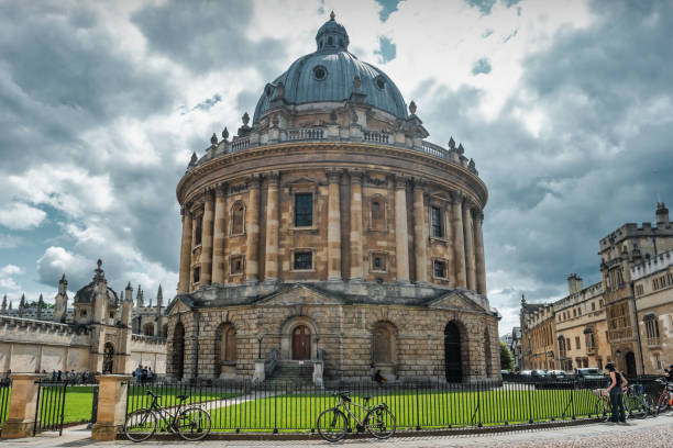Cyclist stands next to Radcliffe Camera, an academic library of the University of Oxford, in central Oxford, England, UK on a cloudy day.