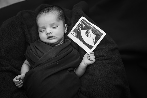 newborn baby holding ultrasound copy in hand and sleeping at mother palm in black and white