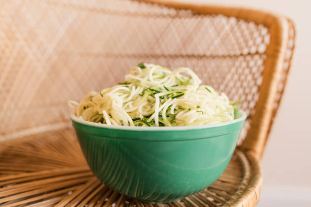 vibrant vintage teal borosilicate glass bowl filled with zucchini cut into spaghetti-shape sitting on a vintage rattan chair, ready for a healthy summertime dinner - crystal noodles imagens e fotografias de stock