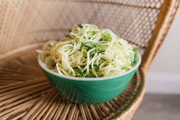 vibrant vintage teal borosilicate glass bowl filled with zucchini cut into spaghetti-shape sitting on a vintage rattan chair, ready for a healthy summertime dinner - crystal noodles imagens e fotografias de stock