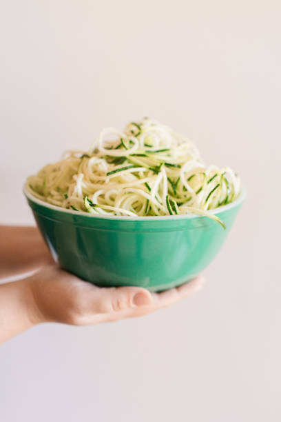 woman holding a vintage teal borosilicate glass bowl filled with zucchini cut into spaghetti-shape, ready for a healthy summertime spaghetti dinner - crystal noodles imagens e fotografias de stock