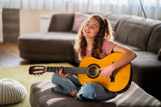 Happy girl plying guitar at home stock photo