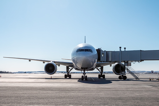 Front view of the white wide body passenger aircraft at the boarding bridge on the airport apron