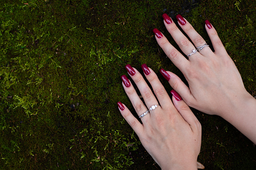 The hands of a young girl show a red cherry manicure on her  fingers nails against the background of moss