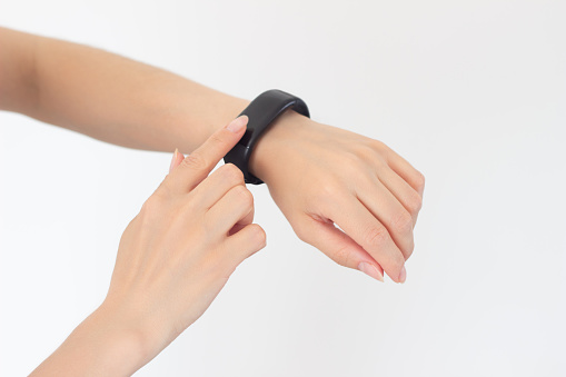 young woman monitors her health, uses a fitness bracelet by pressing them with her index finger and checks her pulse and the number of steps. Isolated on a white background