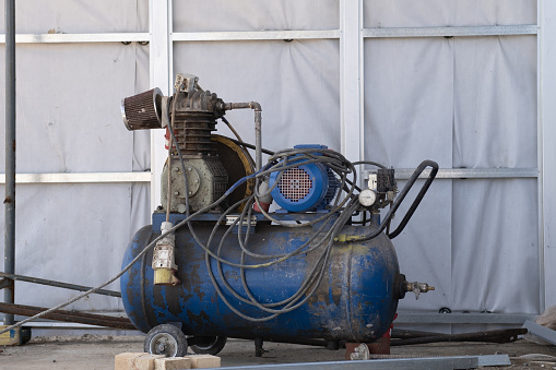 An old blue Working mobile air compressor for painting walls on a construction site. Engineering equipment.