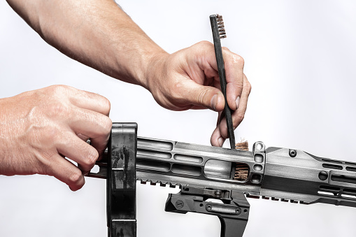 Man`s hands holding rifle parts details and cleaning the gun by metal brush grey background
