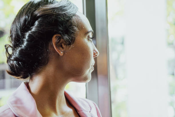 istock Young woman contemplating and looking through the window 1634304254
