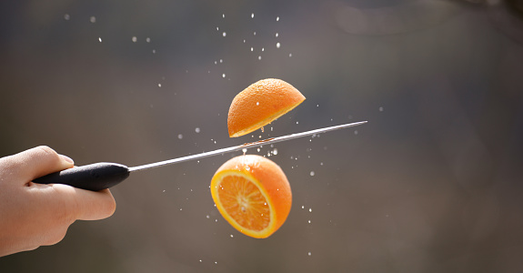 stainless steel  knife cutting orange fruit and splashing water mid air