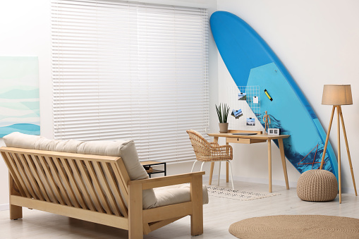 SUP board, workplace and sofa in room. Interior design