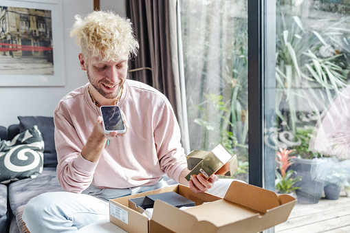 A young Caucasian man is cheerfully talking on the phone, while checking out the contents of his package delivery.