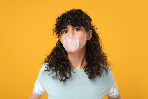 Beautiful young woman blowing bubble gum on orange background