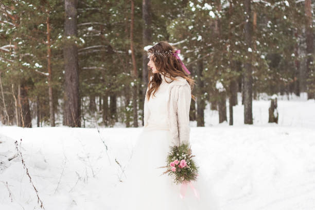 Beautiful bride in a white dress with a bouquet in a snow-covered winter forest. Portrait of the bride in nature stock photo