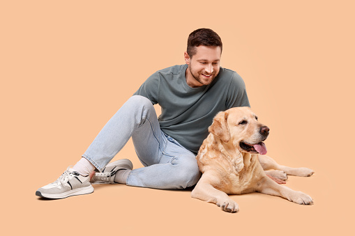 Man with adorable Labrador Retriever dog on beige background. Lovely pet