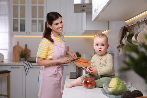 Happy young woman with her cute baby spending time together in kitchen