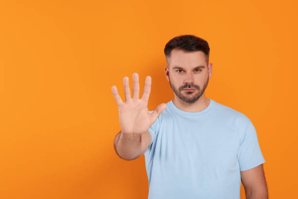 istock Handsome man showing stop gesture on orange background, space for text 1634429145