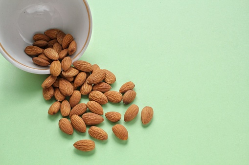 Almond nut on white ceramic bowl on green background. Healthy eating diet, nutrition, vegan concept. Protein organic food. Dry snack. National nut day. Copy space for text