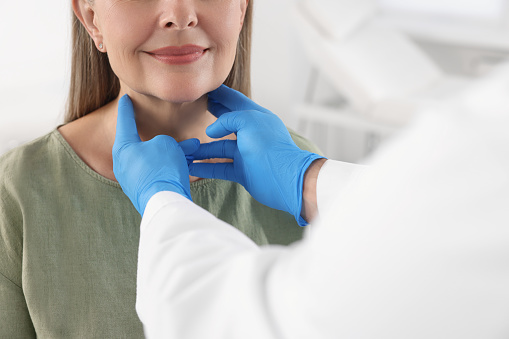 Endocrinologist examining thyroid gland of patient indoors, closeup