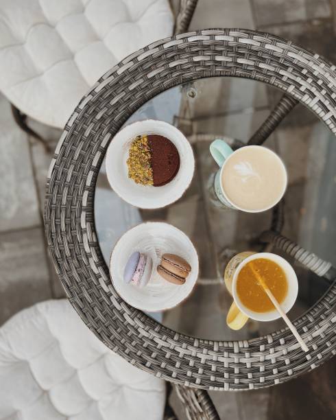 Coffee latte, sea buckthorn tea, macarons and choco pie on the table made of artificial rattan and glass