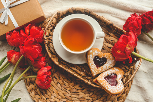 Tray with tasty breakfast, bouquet of peonies and gift for Valentine's Day on bed.