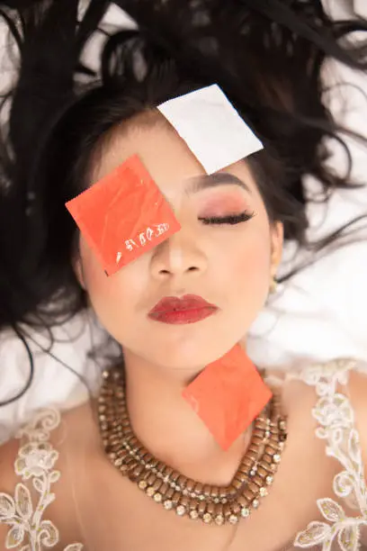 an Asian woman with a gold necklace falls asleep with a condom wrapper on her face in a hotel at night